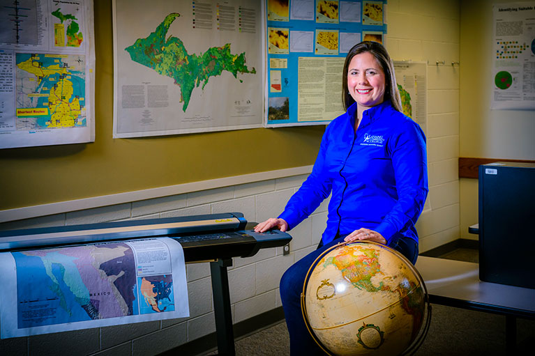 LCC Geography instructor posing with a globe for a photo in a classroom