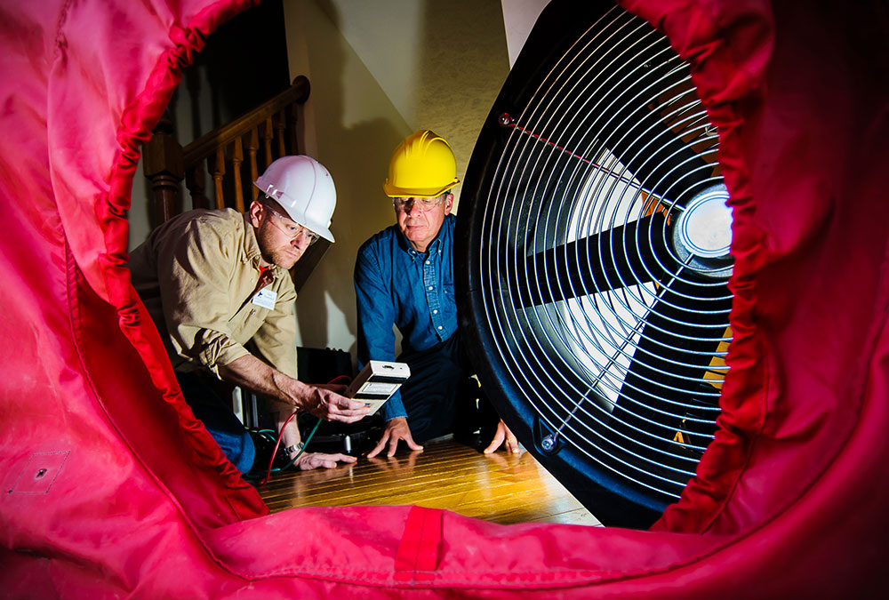 two men looking at a fan blowing into a round tube during energy management experiment