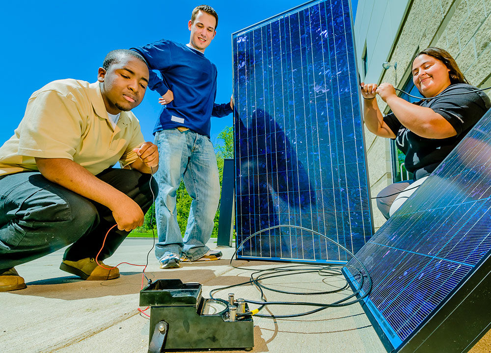 three students working on an solar energy panel outside