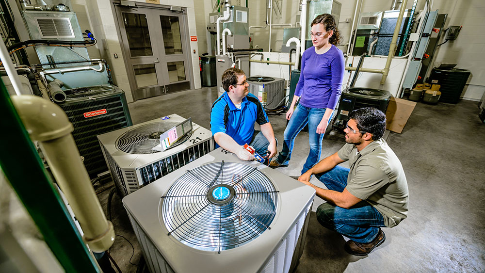 two students and an instructor looking at a central air system