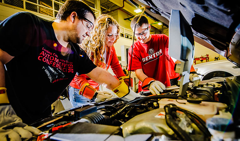 three automotive technology students looking under hood of car