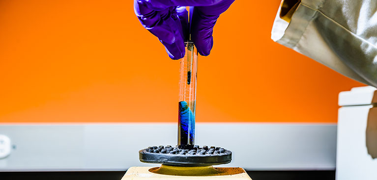 close up of chemists hand while doing an experiment with small glass beaker