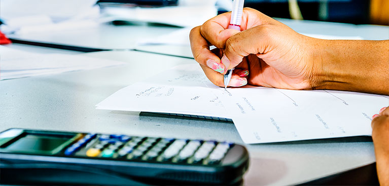 close up of student's hand writing and using calculator during a mathematics class