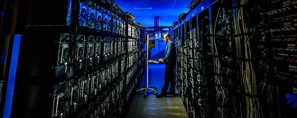 man looking at his laptop inside a room of servers