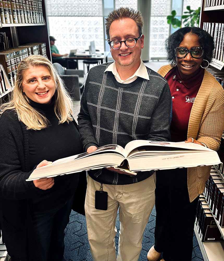  Ami Ewald, John Szilagyi, and Robin Moore holding a large book together