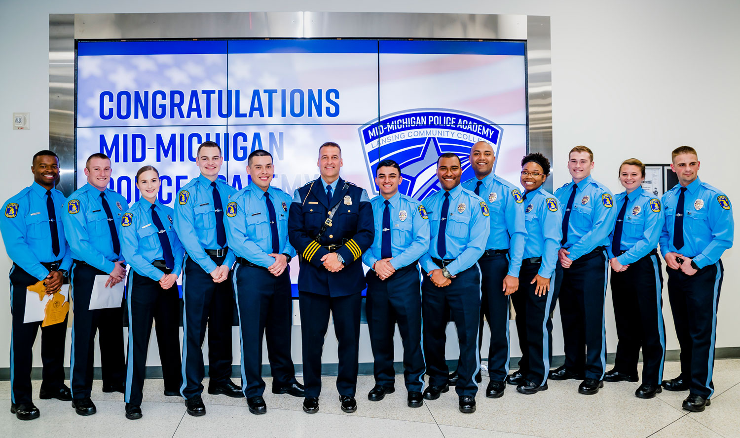 group of police academy graduates in a row for a photo with the lansing police chief