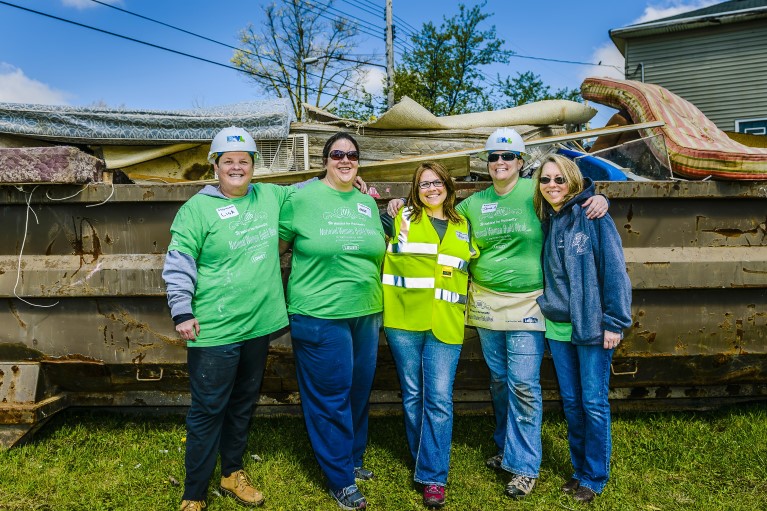 Four women in hard hats and construction vests stand in front of a contruction site.