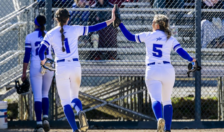 Two women in LCC softball uniforms high five as the leave the field.