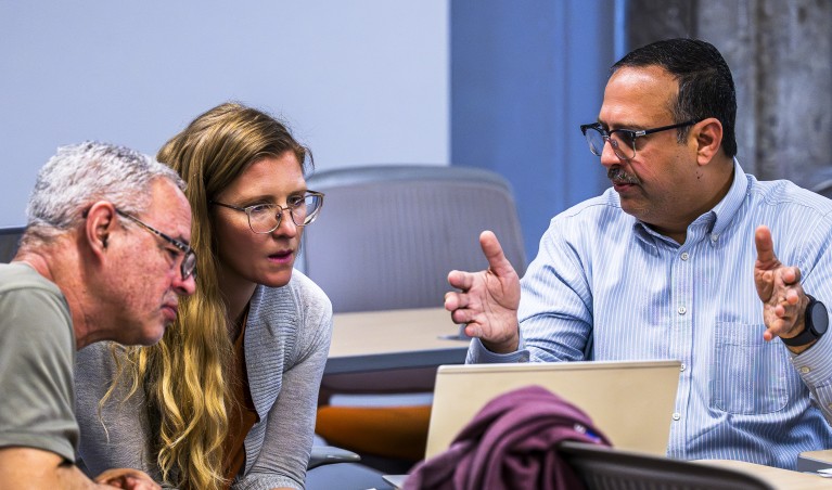 Students engage in a conversation while looking at a laptop in a classroom.