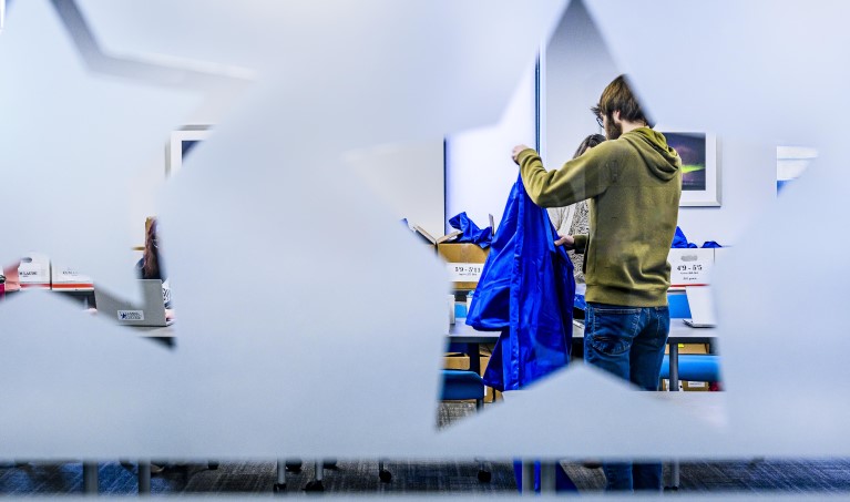 A student selects a blue graduation gown as seen through a star shaped opening in frosted glass