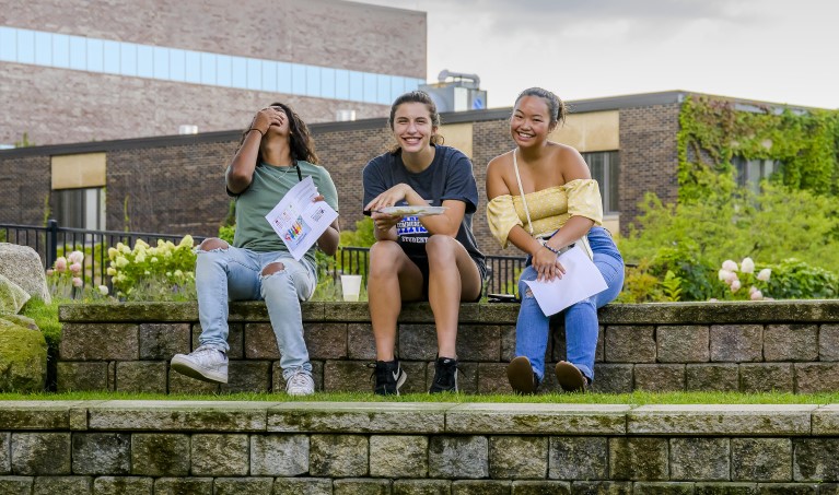 Three students sitting together outside on grassy steps.
