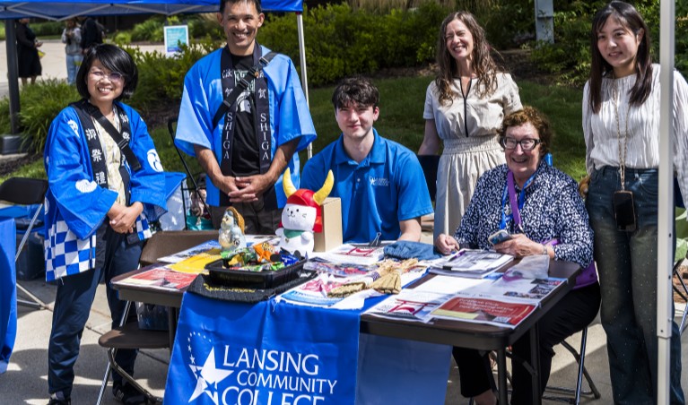 Three phi theta kappa students and three faculty sitting and standing at an information table outside on campus