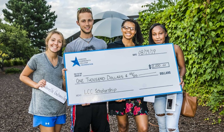 Four students standing with an oversized check made out to scholarships