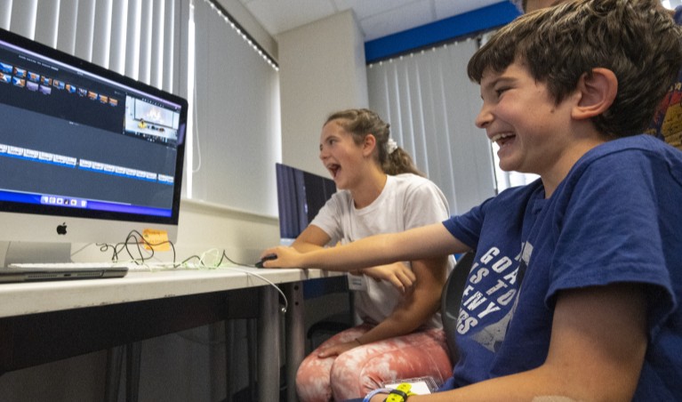 children laugh as they work together at a computer.