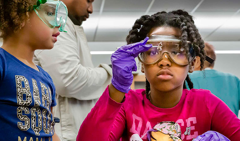two children with safety glasses on inspecting something up close in a youth science program classroom