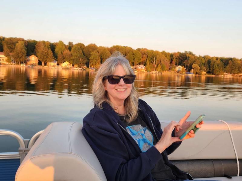 amy park holding her phone on a boat in a lake during sunset