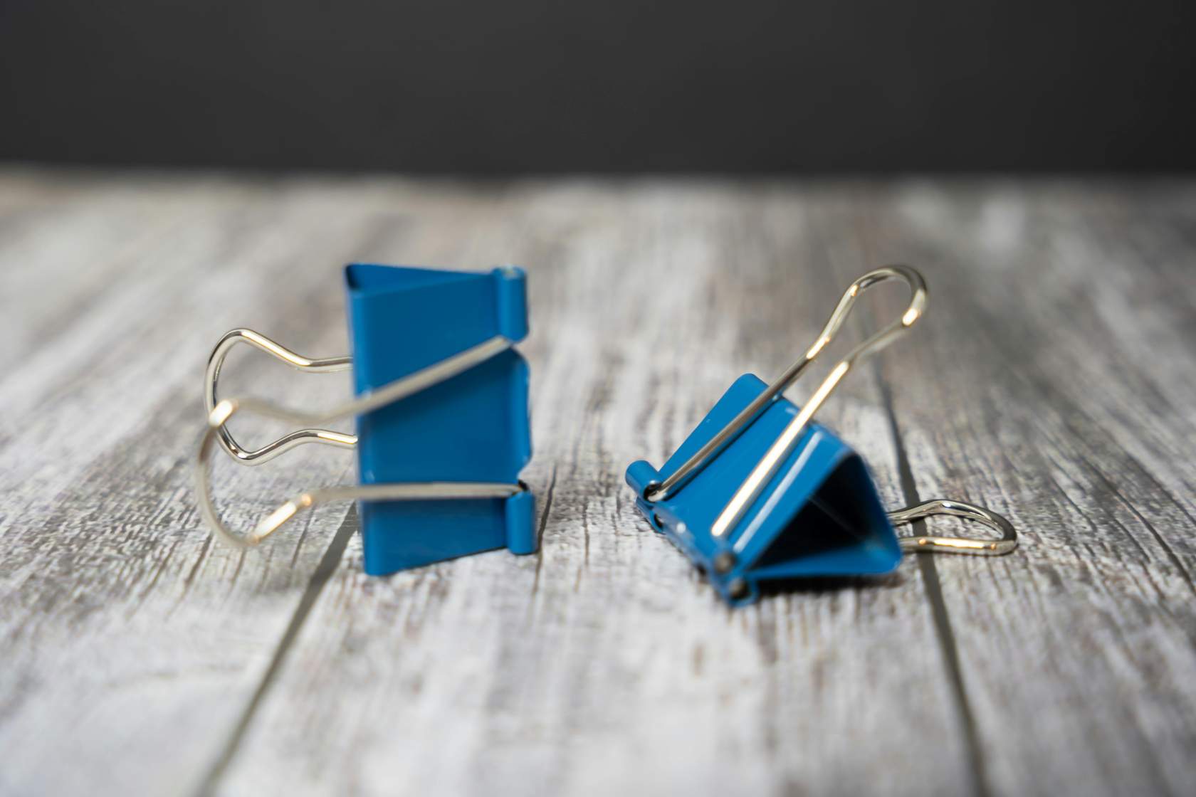 two blue paperclips on a wood table