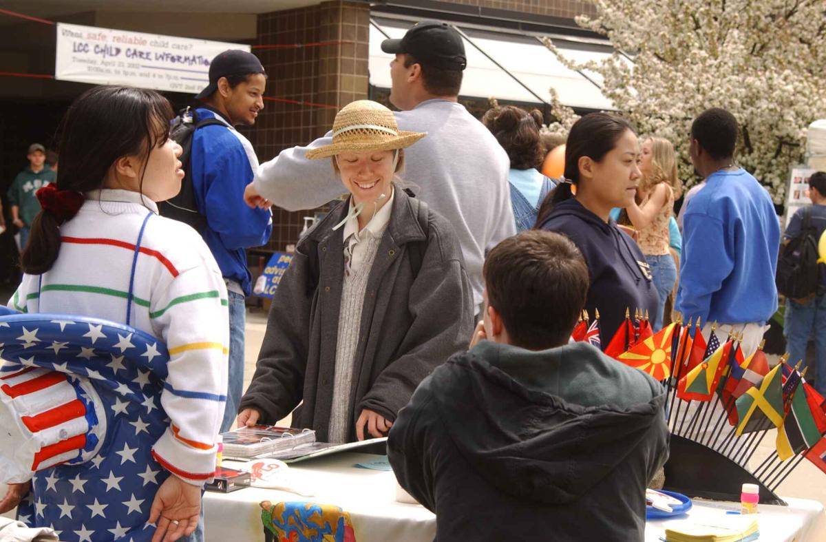 A person in a hat talks to two people at a table with many little flags from different countries.