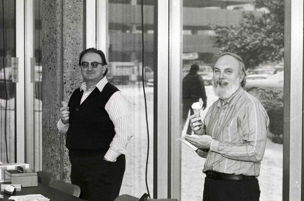 Two men stand outside holding ice cream cones.