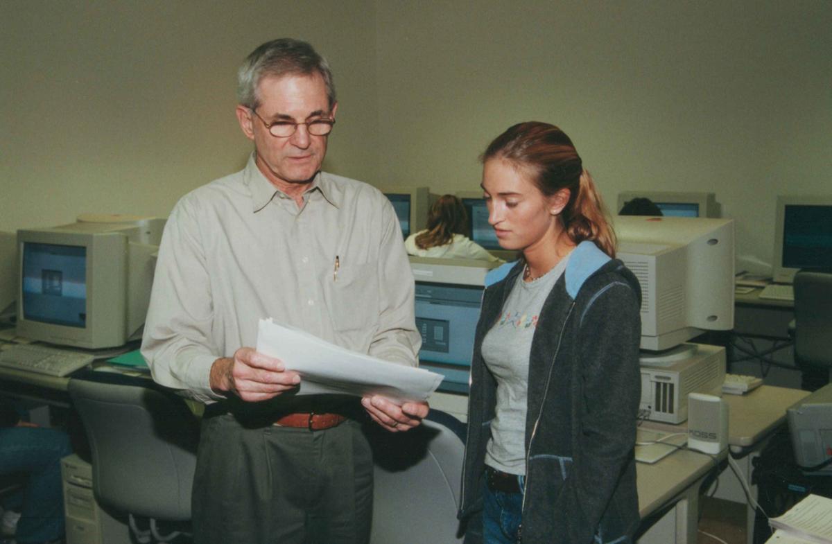 A man and woman look at a piece of paper in a computer lab.