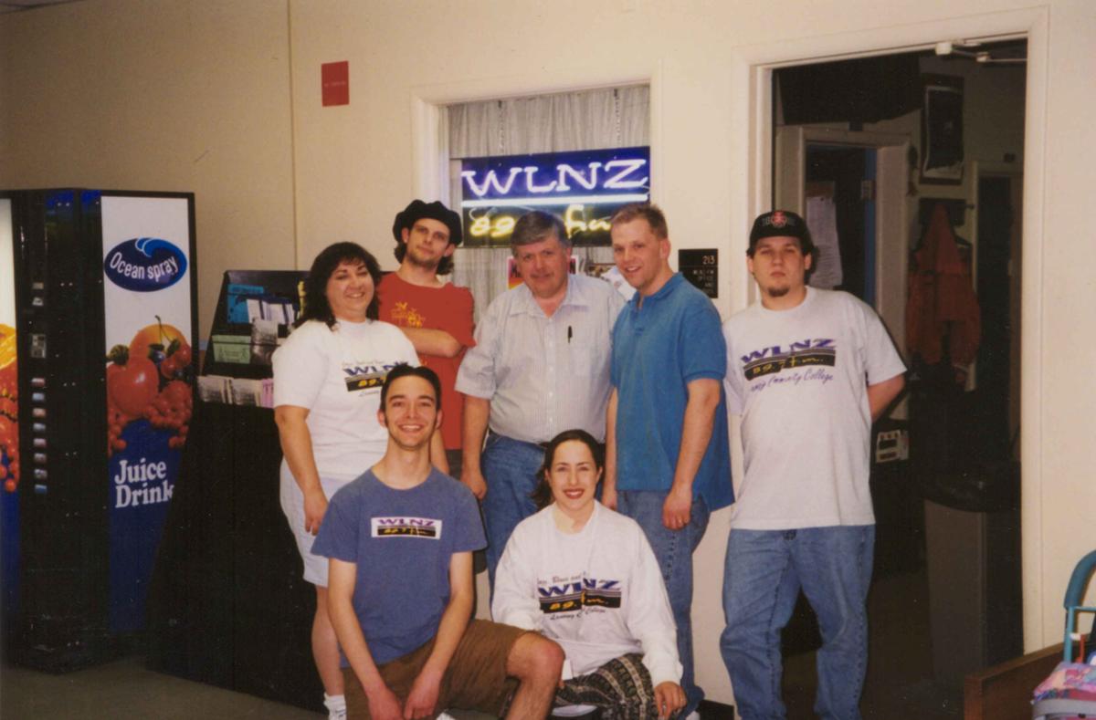 A group of people stand in front of a neon sign that says, "WLNZ."