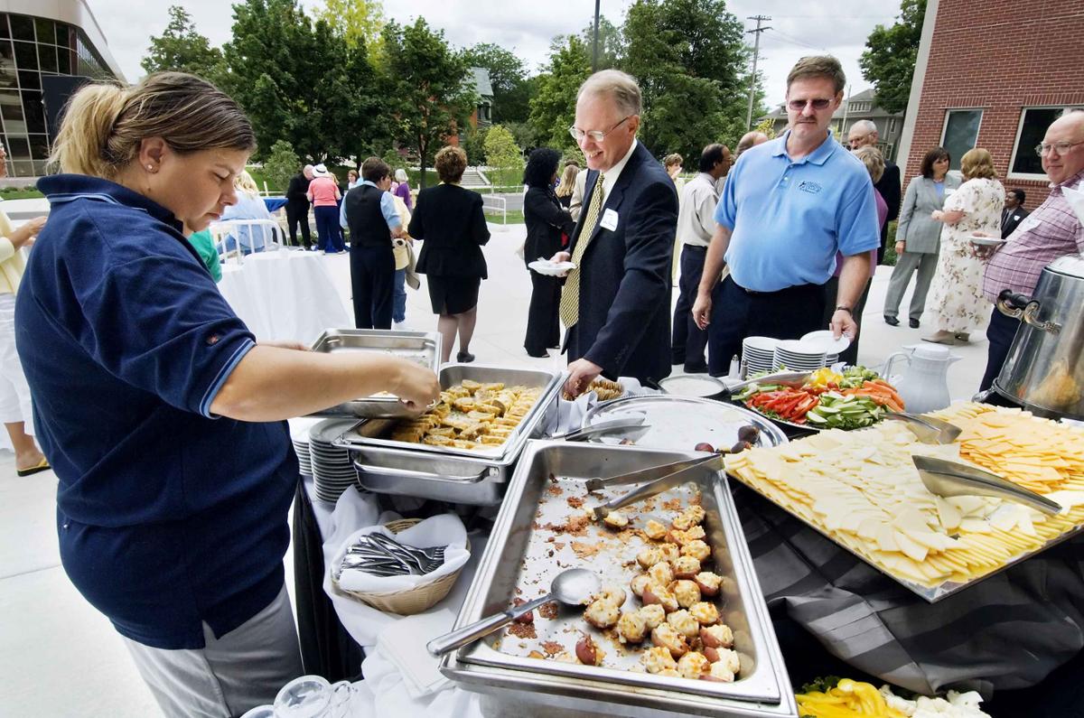 A group of people stand outside the Admin building in front of a buffet table. People mingle in the background.