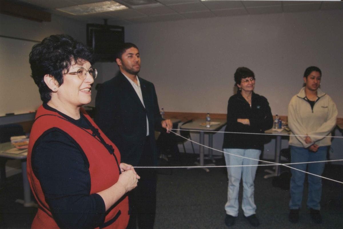 Four people stand in a room. Two of the people are holding a string that looks to be spread out across the room to others not in the picture.