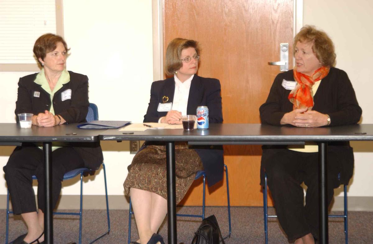 Three women sit at a table. One woman is speaking.