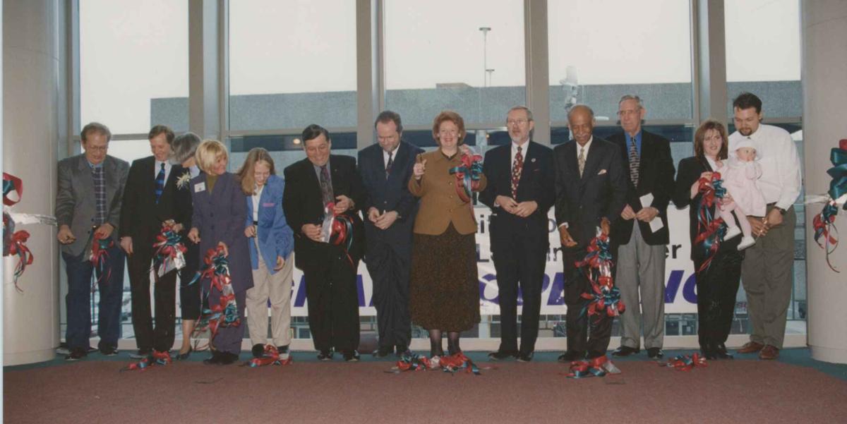 A group of people stand in front of a window. Many of the people are holding red and green ribbons.