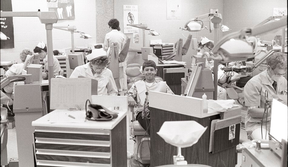 A young patient smiles while sitting amidst Dental Hygiene students working in the Dental Clinic in the Arts and Sciences Building - ca. 1980s