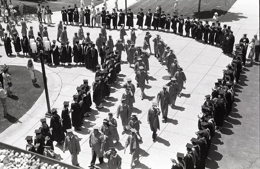 Faculty and staff line the sidewalk leading to the Gannon Building and applaud the graduate procession from the Arts & Sciences Building - ca. 1980s