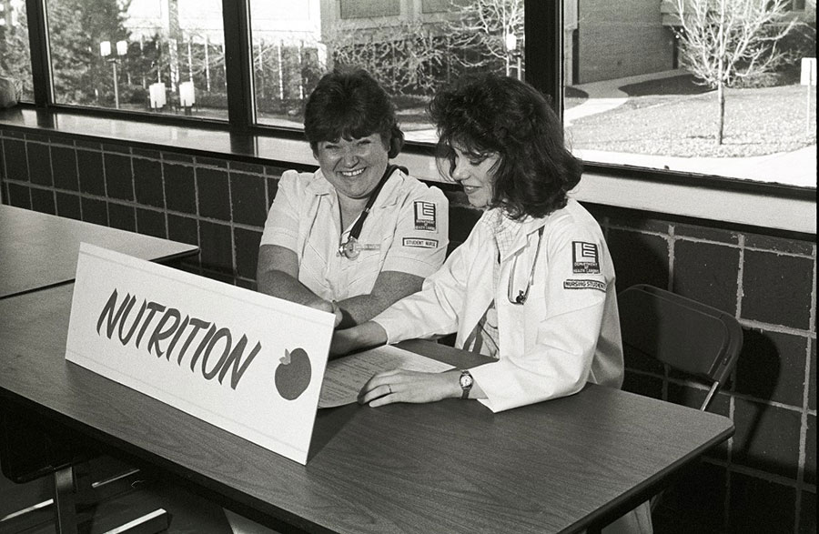 Students from the Department of Health Careers sit at the "NUTRITION" table at a health fair in the Gannon Building - ca. 1980s