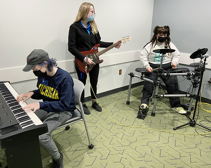 students playing drum set, keyboard, and guitar in the music and voice recording room