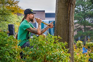 man playing an instrument outside next to a tree on lcc campus