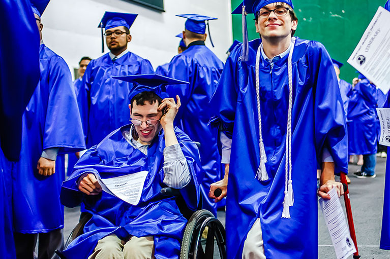 Two men at graduation commencement - one in a wheelchair and one standing