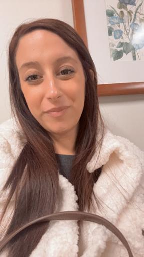 Sophia A photo of student, Sophia. It shows her head and shoulders and she is closed-mouth smiling at the camera with a white wall and framed floral art behind her.