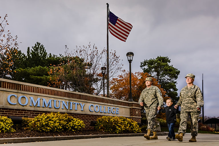 Two veterans stroll with a child passed the LCC sign and an American flag
