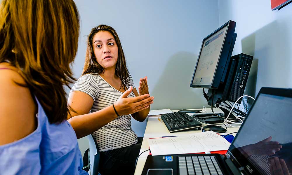 Student sitting at computer and talking to advisor