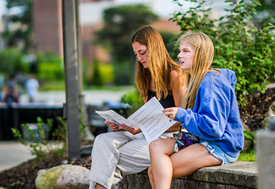 two students looking at papers outside